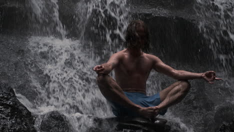 young man meditating under waterfall.