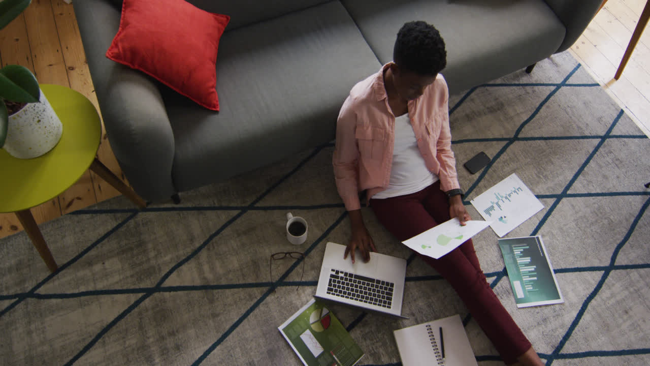 African american woman holding a document and using laptop while working from home