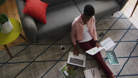 African-american-woman-holding-a-document-and-using-laptop-while-working-from-home