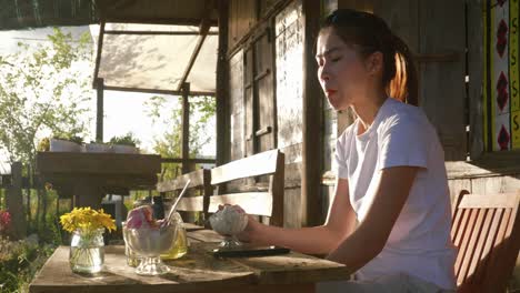 Asiatische-Frau-Sitzt-Am-Hölzernen-Picknicktisch-Auf-Der-Veranda-Und-Isst-Eis,-Vietnam