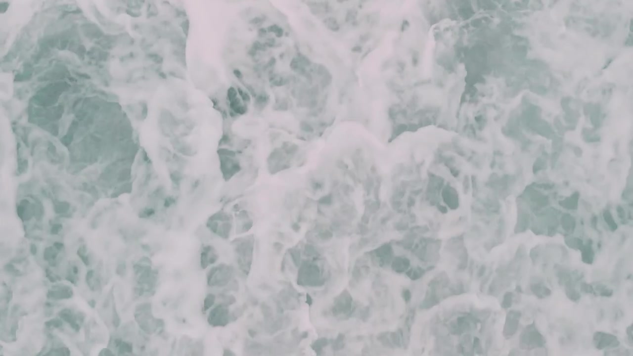 Vista aerea di onde oceaniche che si infrangono su una spiaggia di sabbia scura.