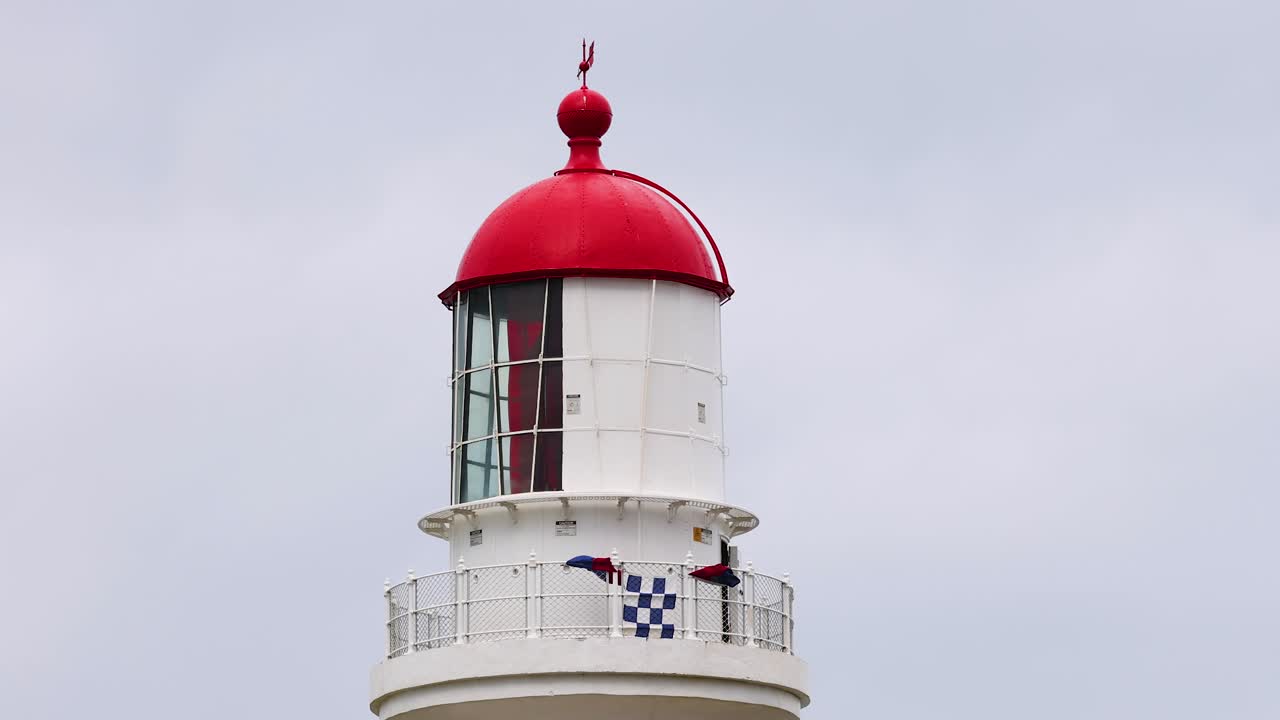 A serene view of a lighthouse with a red dome against a cloudy sky, captured at Aireys Inlet, Victoria