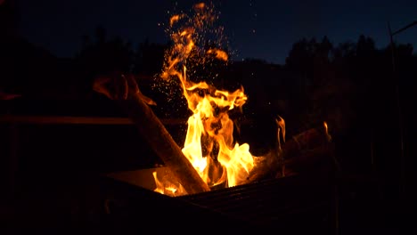 Vibrant-yellow-flames-and-sparks-while-stoking-campfire-at-night-in-slow-motion