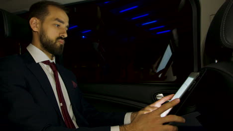 hombre de negocios trabajando en su portátil en el asiento trasero de su coche de lujo con conductor personal