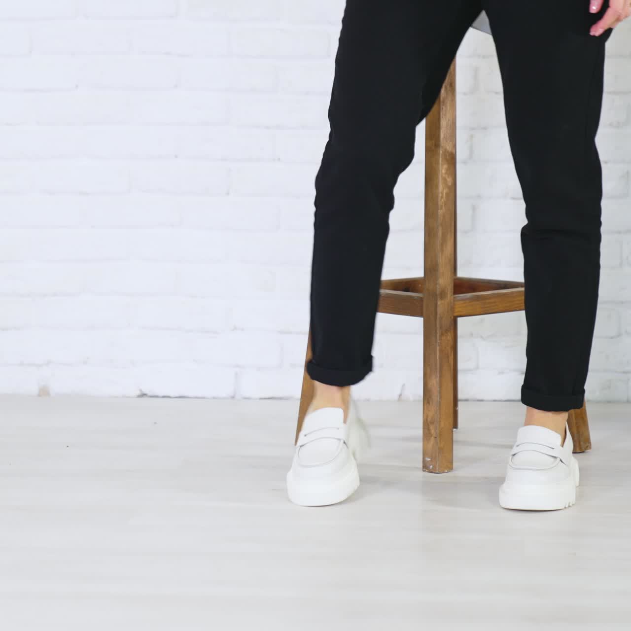 Fashionable white shoes presentation. Female model walks in fashionable footwear back and forth near the wooden tabouret