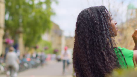 Female-Tourist-On-Vacation-In-Oxford-UK-Exploring-City-Walking-Along-Broad-Street-Taking-Photo-With-Mobile-Phone-1