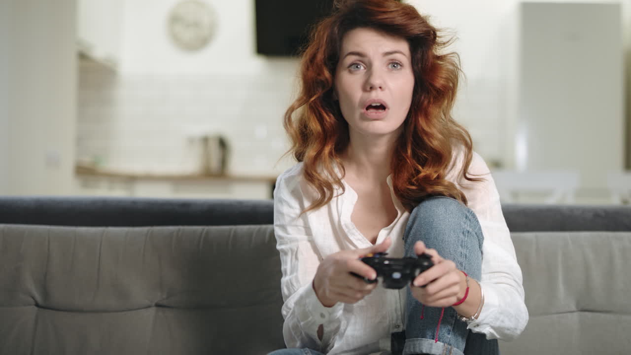 Energisk kvinde spiller videospil i hjemmekøkkenet. Smuk pige holder PlayStation.