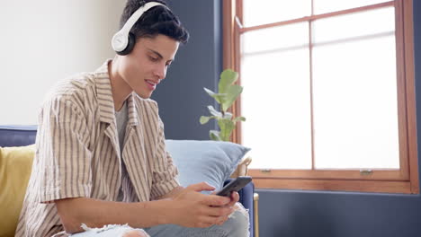 happy biracial man wearing headphones listening to music using smartphone, copy space, slow motion