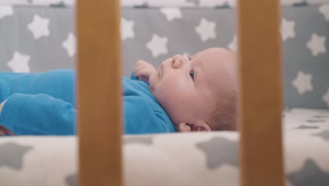 newborn boy in azure bodysuit moves hands resting in crib