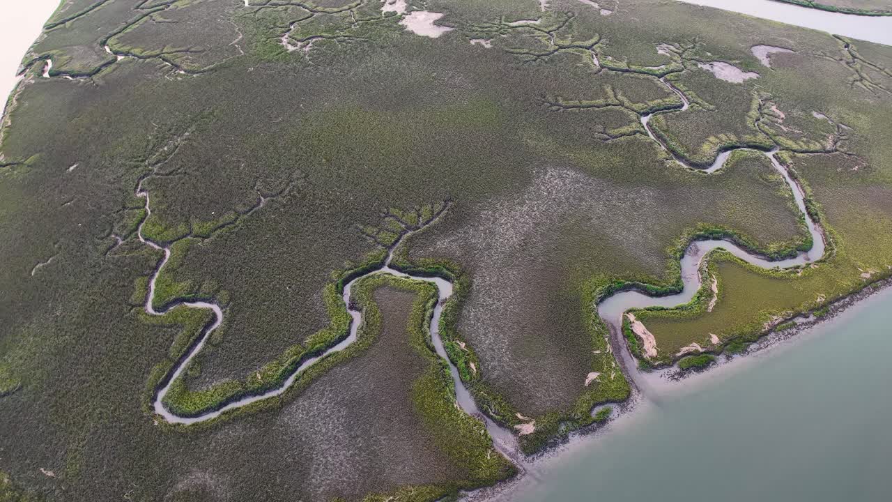 Drone footage of winding waterways through green marshland along a coastal island shoreline