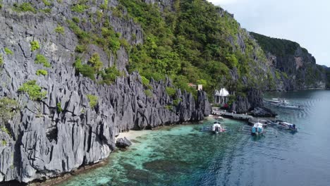 tour boats at pier of old catholic shrine abandoned resort hidden behind limestone mountain rocks with tropical clear blue water at mantiloc island el nido philippines