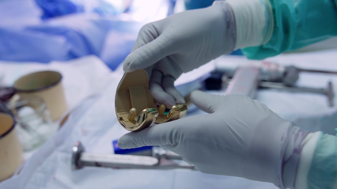 Hands of doctor in latex gloves holding a knee prosthesis. Materials for knee joint replacement. Close up.