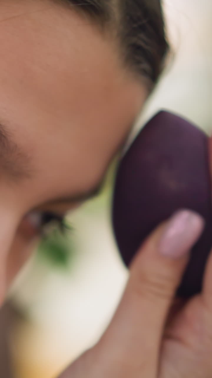 Close shot of woman applying makeup carefully, Female artist gently dabbing foundation onto cheek with sponge tool, Focused woman uses soft strokes to apply base makeup with pink manicure tool