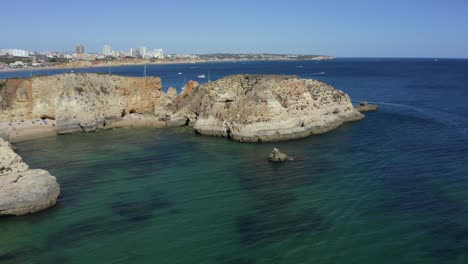 Drone-flies-over-epic-ocean-cliffs-surrounded-by-warm-tropical-exotic-ocean-water-with-sail-boats-and-yachts