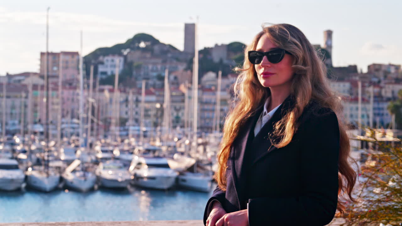 Kvinne med solbriller smiler foran båter som ligger til kai i Pierre Canto-havnen i Cannes, Frankrike