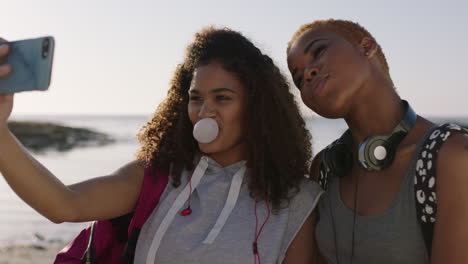 two friends taking selfies blowing bubblegum having fun on sunny beach