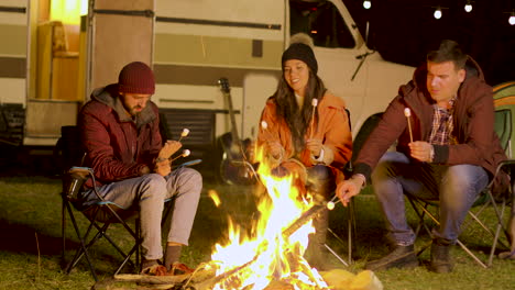 friends relaxing around camp fire and roasting marshmallows on sticks