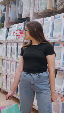vista trasera de una compradora caminando por el pasillo del centro comercial, llevando bolsas de compras mientras mira los productos en el estante, el cabello largo fluye mientras se mueve en un entorno minorista bien iluminado