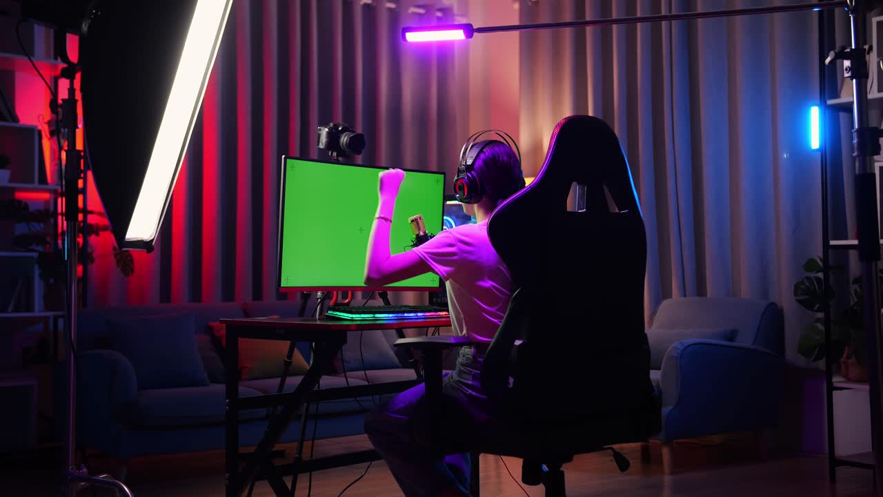 vista trasera de la chica asiática streamer gritando gol y bailando celebrando el juego ganador en la computadora de pantalla verde. videojuego de transmisión en vivo, escritorio iluminado por luz de tira de led rgb