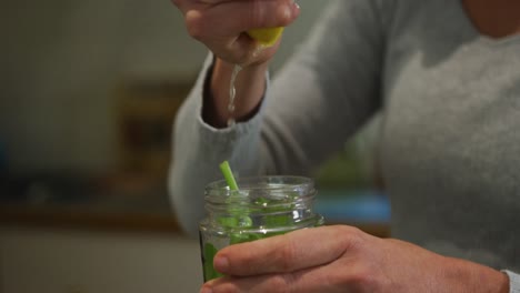 mujer caucásica exprimiendo limón y preparando batido de verduras verdes en la cocina