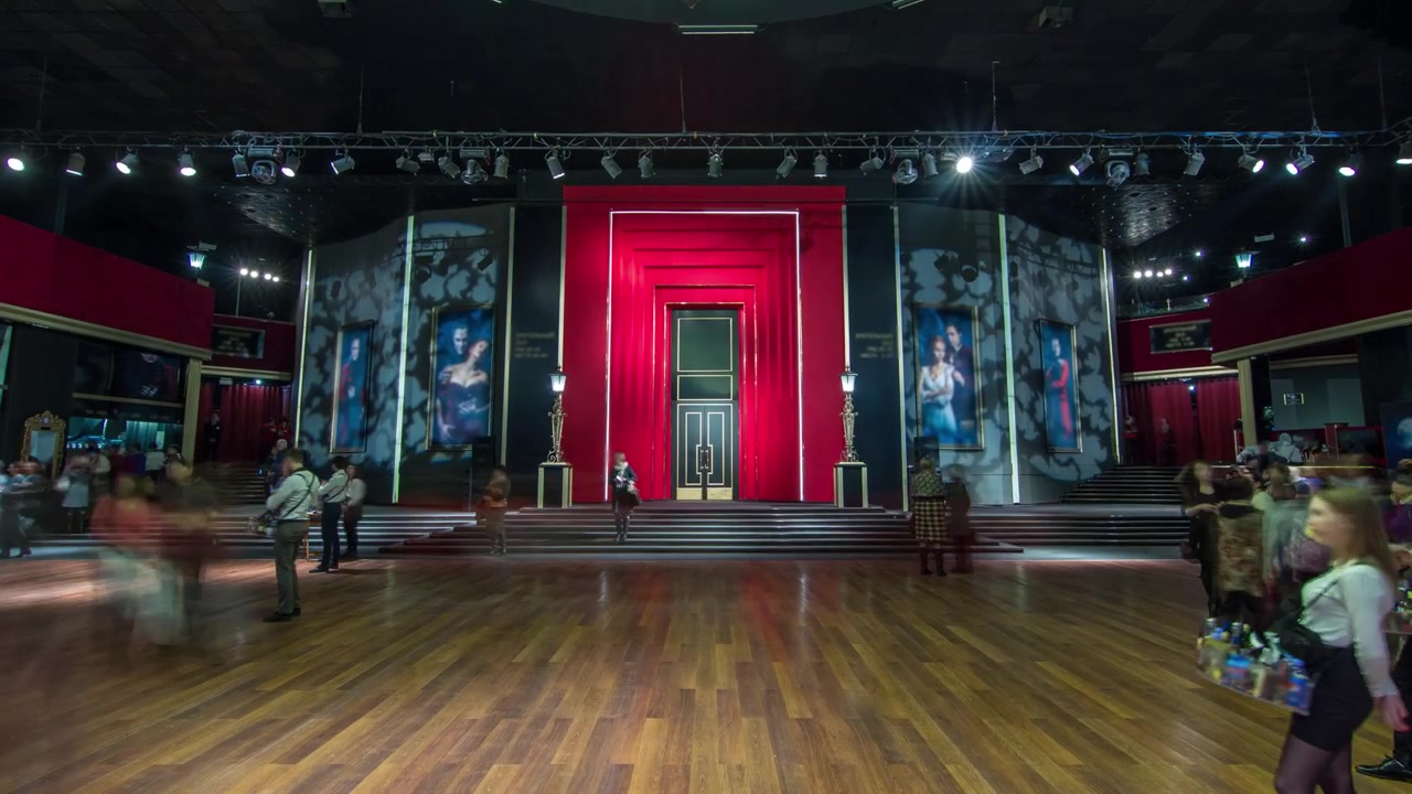 Timelapse hyperlapse de una hermosa y elegante sala de parqué en un teatro. La gente se reúne en la sala antes del espectáculo, y hay movimiento hacia la entrada principal del escenario