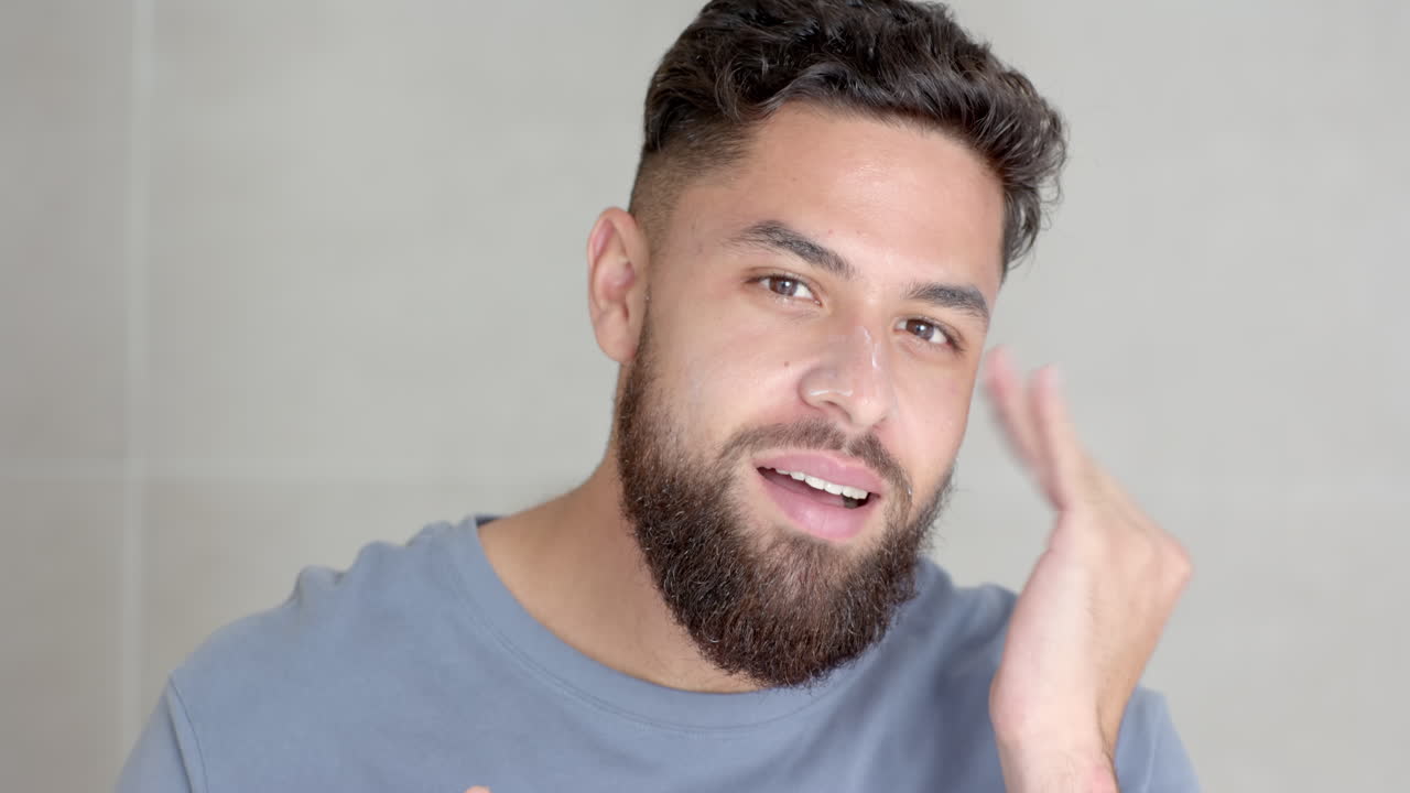 Applying skincare product, man with beard grooming face at home