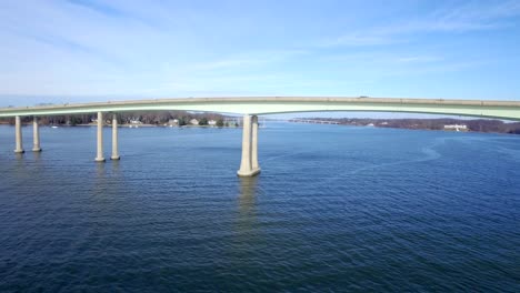 Flying-alongside-a-River-bridge-on-a-clear-blue-day-with-another-bridge-in-the-background-over-blue-water