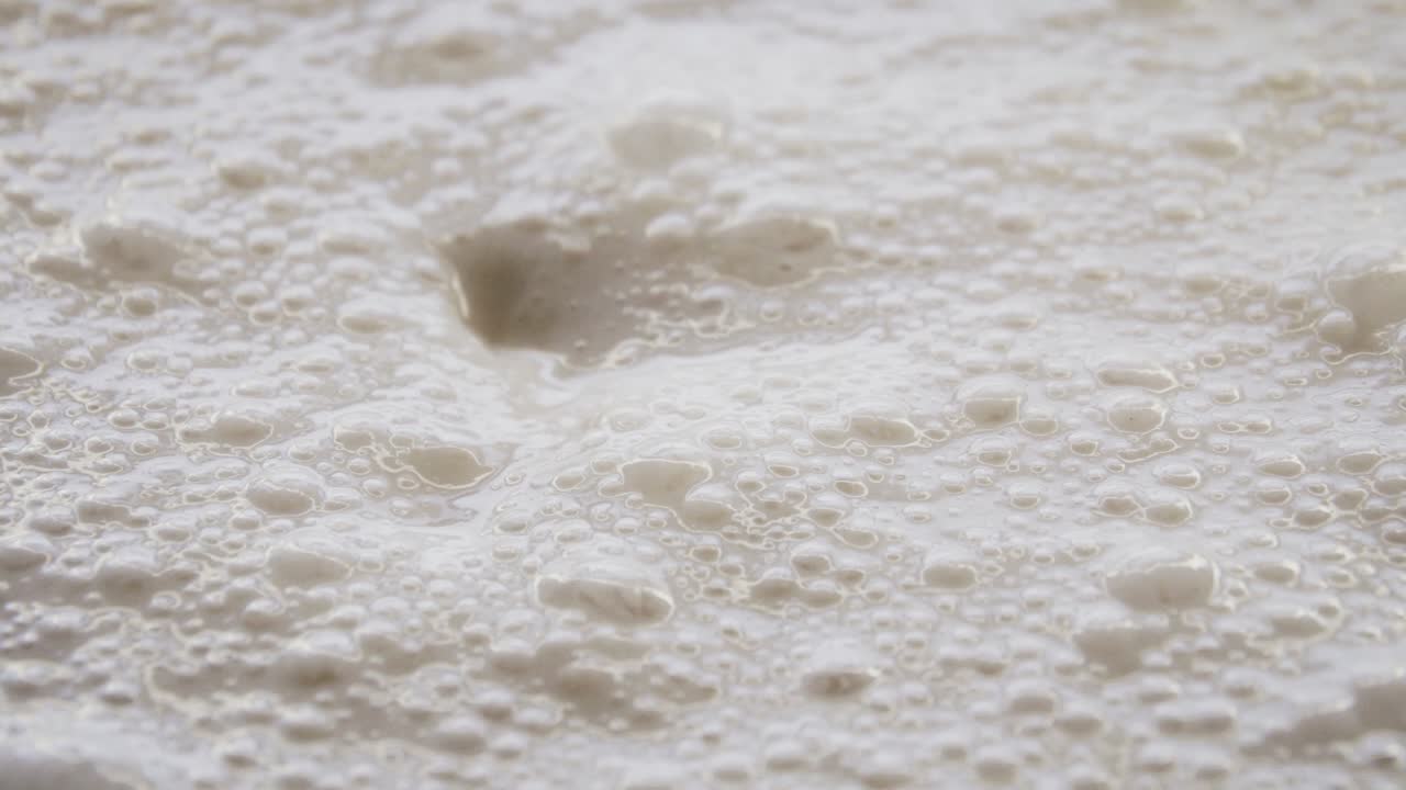 팬케이크를 만들기 위해 그릇에 거품이 이는 효모 제품 덩어리를 숟가락으로 섞습니다.