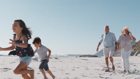 Abuelos-Con-Nietos-Caminando-Por-La-Playa-De-Arena-En-Vacaciones-De-Verano.