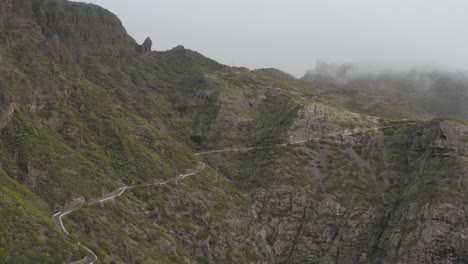 Awe-inspiring-winding-mountain-road-in-rocky-terrain-with-green-foliage-and-low-clouds-brushing-the-mountain-top