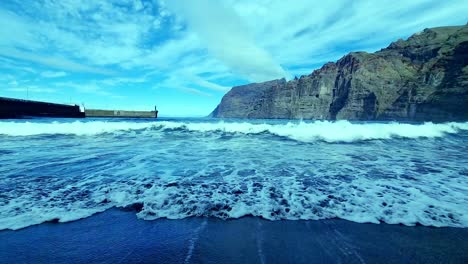 Toma-De-Tierra-De-Olas-Desvaneciéndose-En-La-Playa,-Impresionantes-Montañas-En-El-Fondo,-España