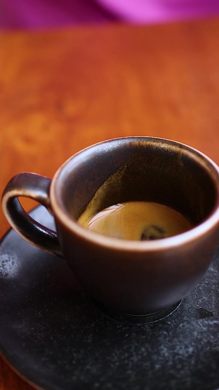 Una mano posa delicatamente una tazzina da espresso in ceramica scura su un piattino nero abbinato.
