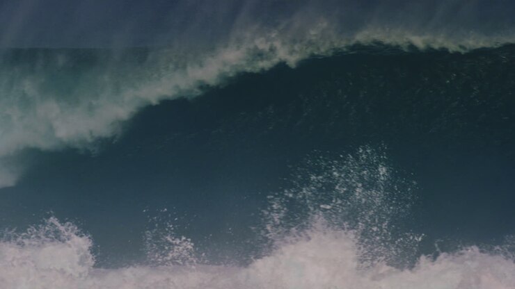Tracking pan follows ocean wave barreling as mist rises in tendrils off top of water in slow motion