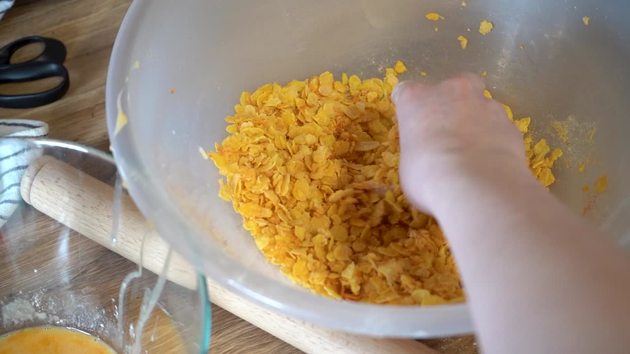 Donna che impana il pollo nei cornflakes.
