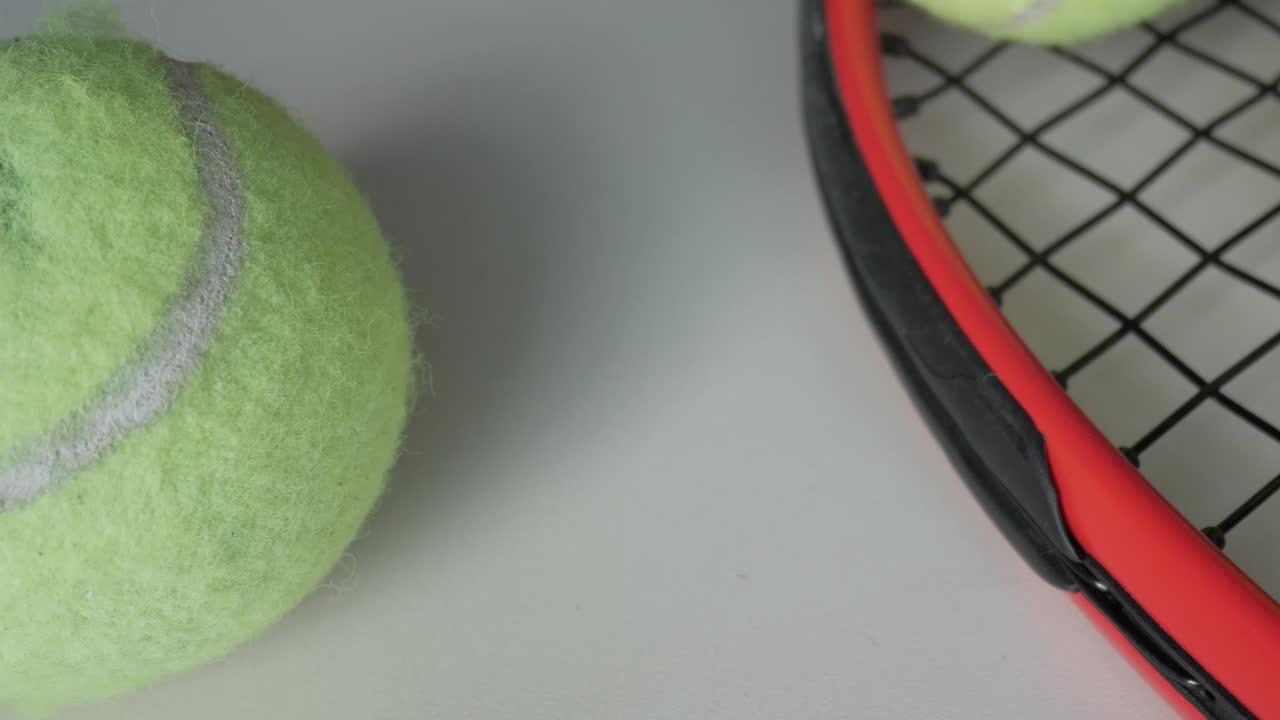 Detailed view of a tennis ball and part of a red tennis racket on a white background, zooming out to reveal more of the scene