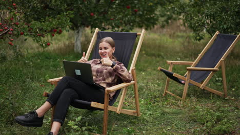 cheerful lady having online video chat and is happy about something. woman rejoices raising her hands and smiling happily. nature at backdrop.