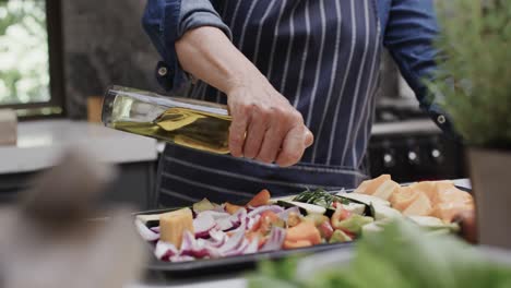 midsection of senior caucasian woman pouring olive oil on vegetables in kitchen, slow motion