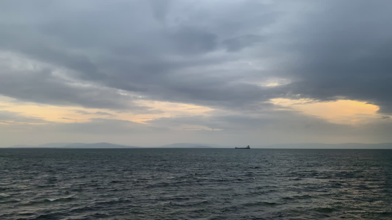 Golden sunset pierces stormy skies over Galway Bay, ship glides toward harbor