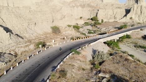 aerial tracking shot behind motorbike driving along empty curved highway road through hingol national park in balochistan desert landscape