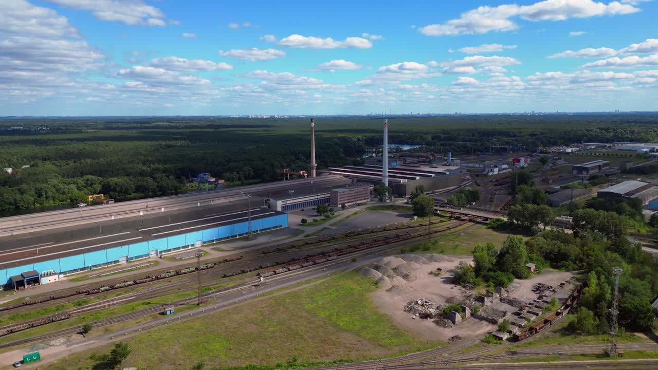 Hennigsdorf steel factory with chimneys, warehouses, railway, near river and forest in summer. Lovely aerial view flight fly reverse drone