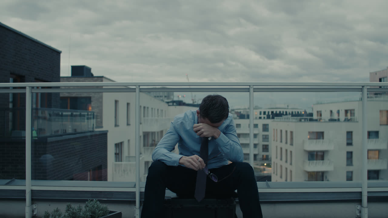 A sad man in a shirt smokes a cigarette on the balcony