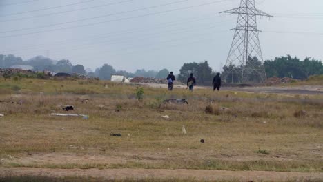 three people walking in a littered field near power lines