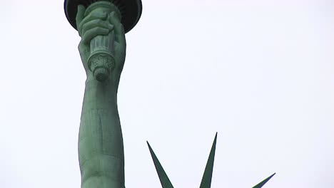 the camera pans from the head and crown of the statue of liberty up to the torch