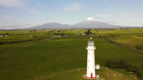 Leuchtturm-Inmitten-Grüner-Weiden-Und-Majestätischer-Taranaki-Kegel-Am-Horizont