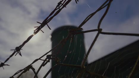 close up shot of fence with barbed wire and tower of popular factory in background