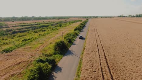 disparo de seguimiento aéreo, de un coche deportivo suv de lujo gris, conduciendo lentamente por una carretera asfaltada de campo, rodeado de campos de trigo dorados