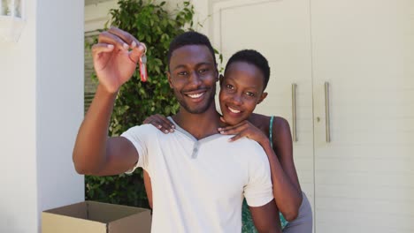 Portrait-of-smiling-african-american-couple-holding-house-keys-and-embracing-outside-their-home