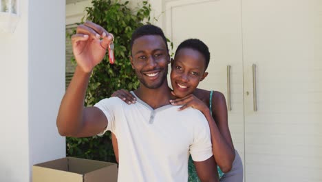 portrait of smiling african american couple holding house keys and embracing outside their home