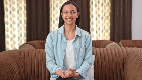 Happy-Indian-woman-sitting-on-sofa-and-smiling