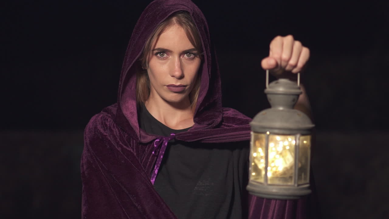 Mysterious role play woman wearing a purple cape and hood and holding a lantern at night